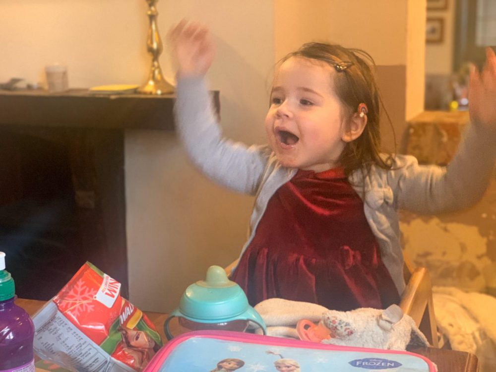 Lottie sat eating at the table with her arms up in the air