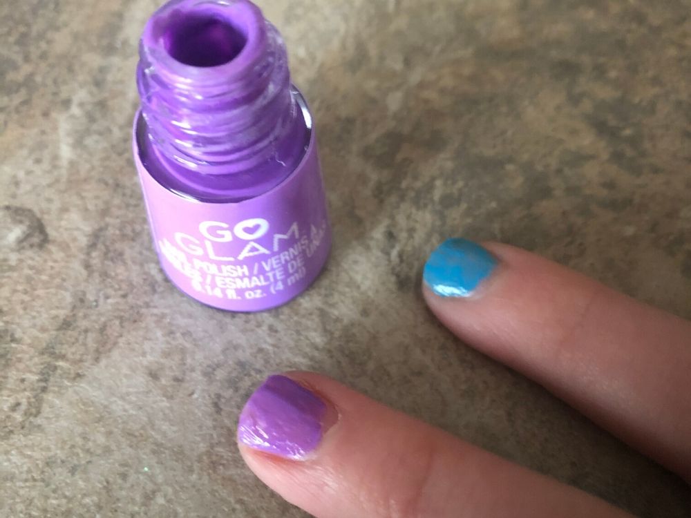 Purple nail polish bottle, purple painted nail and blue painted nail